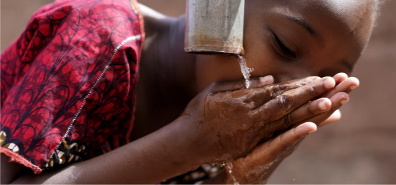 a child drinking from a water faucet to stay hydrated while traveling to malaria risk areas