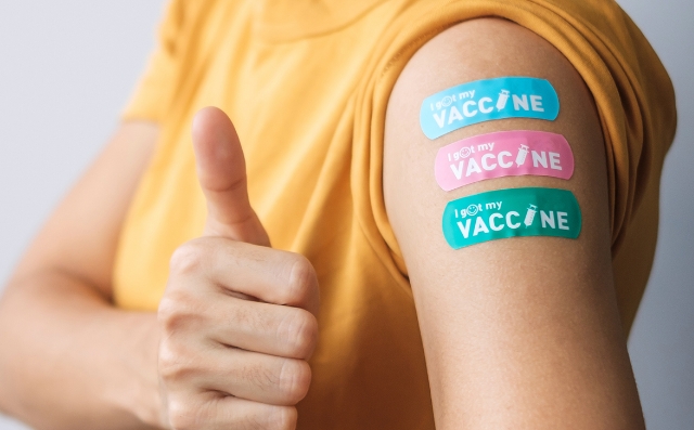 A woman showing thumbs up sign and bandage on her arm after getting travel vaccine